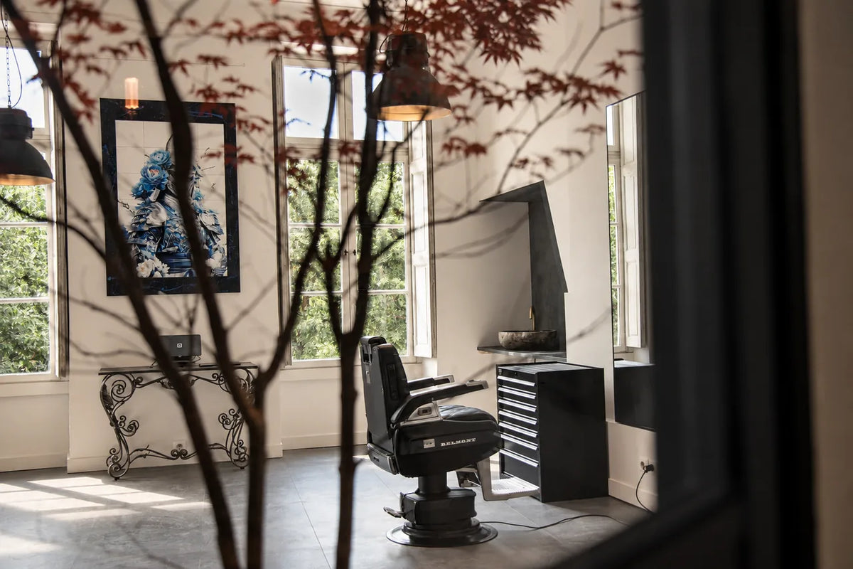 A barber chair in front of the windows at Héritage, seen through maple branches.
