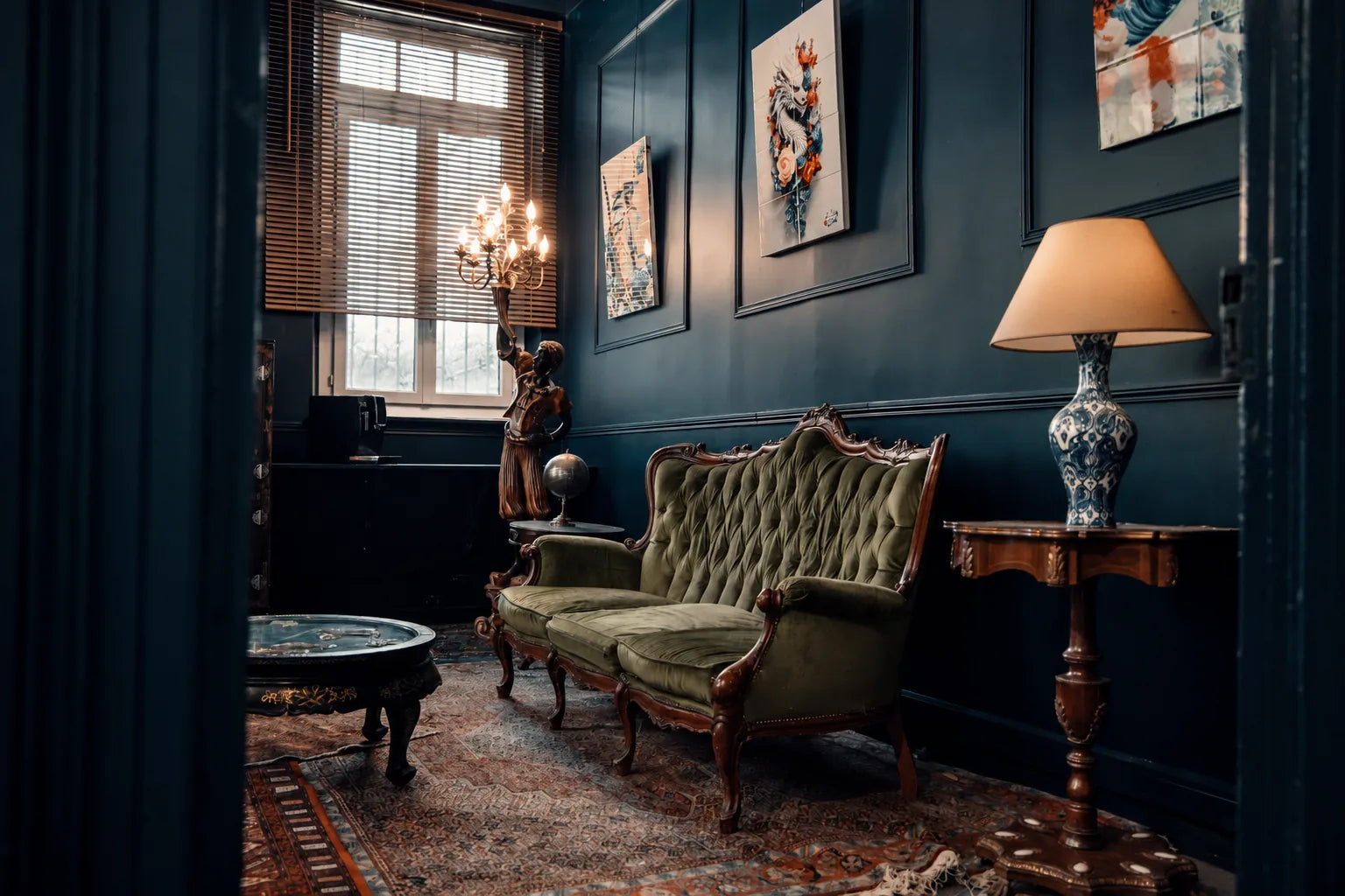 Canapé en velours vert, tableaux et éclairage du salon bleu de la Maison Héritage à Toulouse.