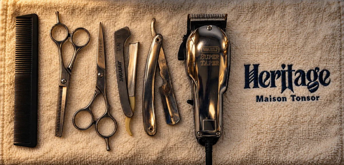 A comb, scissors, straight razors and a clipper on an ivory towel embroidered Heritage Maison Tonsor, in warm light.