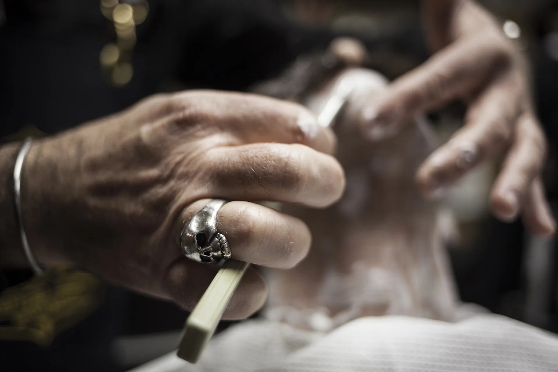Détail de la main du barbier et du rasoir pendant un rasage traditionnel.